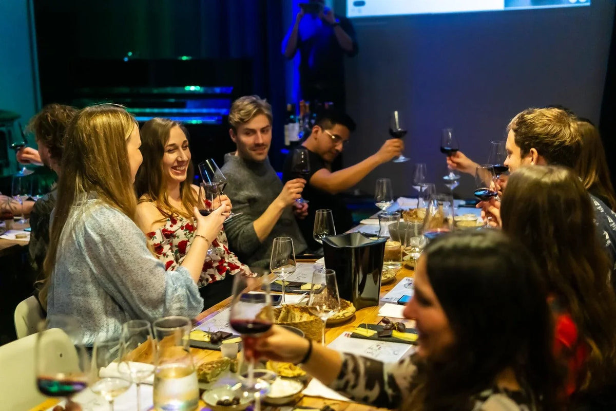 Deltagere skåler med vinglas ved et bord med tapas under en DeVinos-vinsmagning